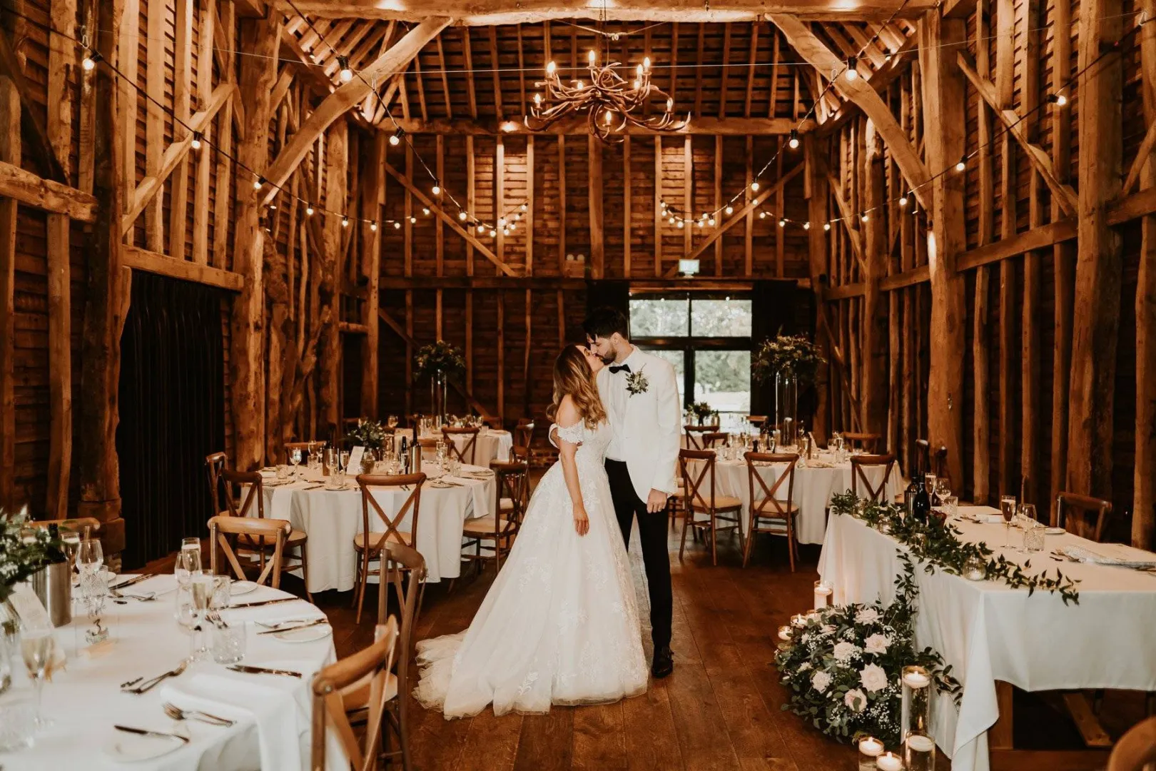 Rustic barn wedding venue featuring elegant wooden beams, twinkling lights, and intimate dining setup with floral accents. Perfect for romantic celebrations.
