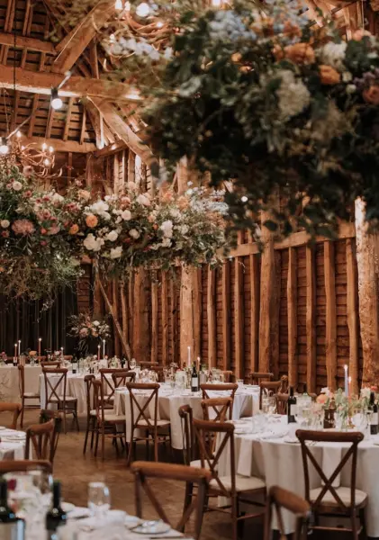 Charming rustic barn venue featuring elegantly arranged tables, twinkling lights, and lush floral installations overhead. Ideal for intimate weddings.