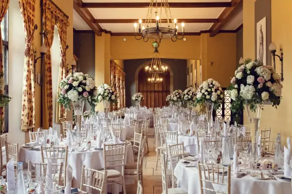 Elegant reception space featuring round tables adorned with white linens and lush floral centerpieces, complemented by warm lighting and rich decor.