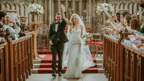 Joyful couple exits a stunning church, surrounded by cheerful guests showering them with flower petals. Elegant wooden pews add charm.