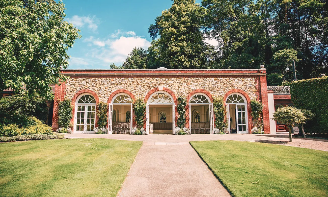 Charming brick venue with arched windows surrounded by lush gardens, perfect for outdoor ceremonies and elegant receptions.