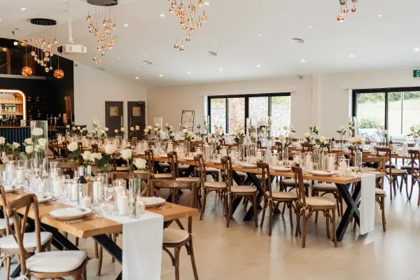 Elegant ballroom featuring rustic wooden tables with floral centerpieces, soft lighting, and large windows for natural light.