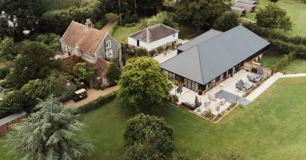 Charming wedding venue featuring a rustic house and modern reception barn surrounded by lush greenery and spacious outdoor areas.