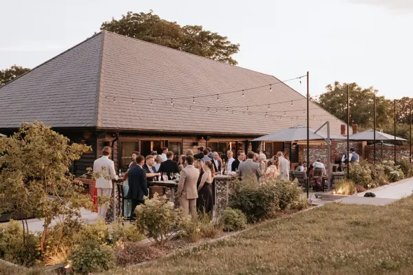 A charming rustic barn with outdoor seating, guests mingling at sunset, and twinkling string lights creating a warm, inviting atmosphere.