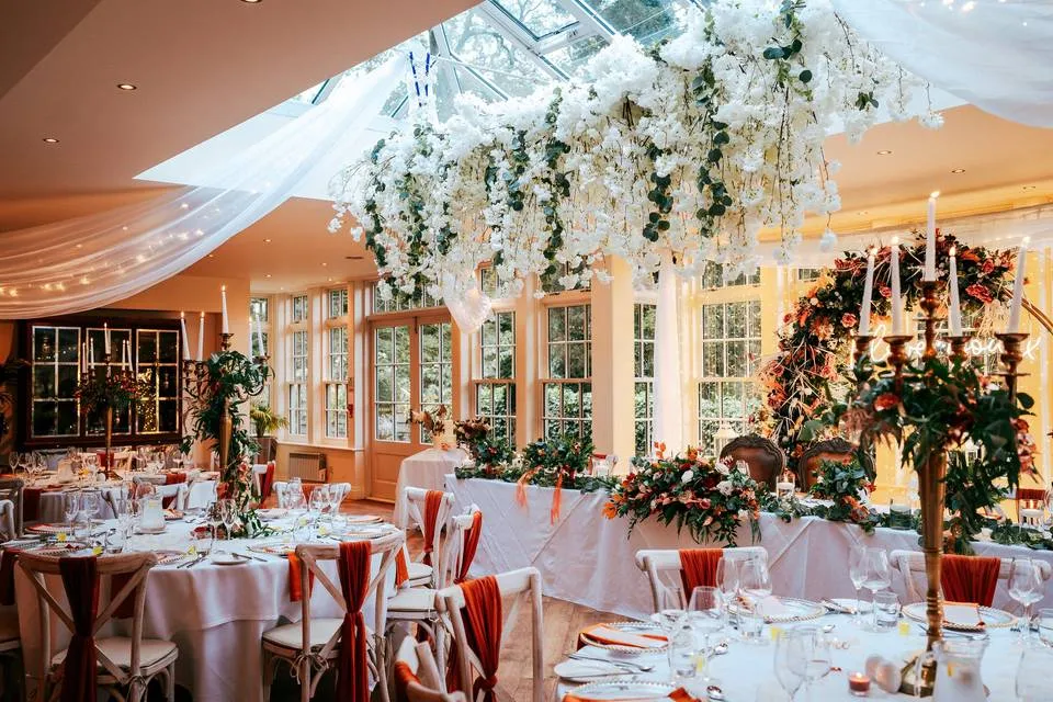 Elegant indoor wedding reception featuring lush floral arrangements, draped ceilings, and beautifully set tables with soft lighting.