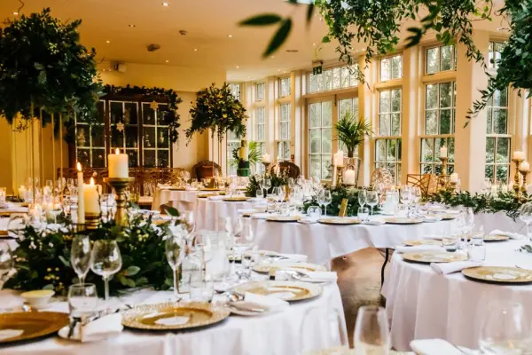 Elegant reception space featuring round tables adorned with greenery, candles, and large windows letting in natural light. Perfect for intimate gatherings.