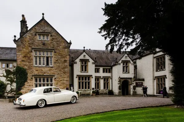 Elegant estate with a classic white vintage car parked in front, featuring charming stone architecture and manicured gardens.