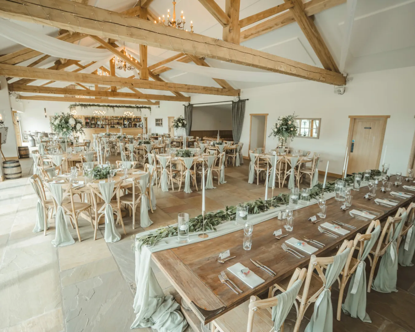 Spacious reception area with exposed wooden beams, elegant table settings, and greenery accents, perfect for an intimate wedding celebration.