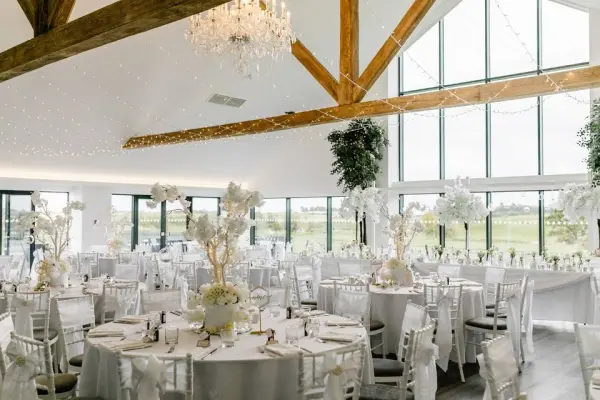 Elegant reception space featuring airy high ceilings, rustic wood beams, and stunning large windows overlooking lush greenery.