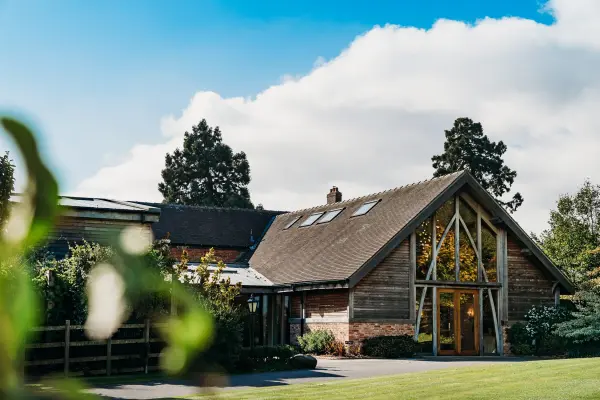 Charming rustic barn featuring large windows and ceiling beams amidst lush greenery and a clear blue sky, ideal for a cozy wedding setting.