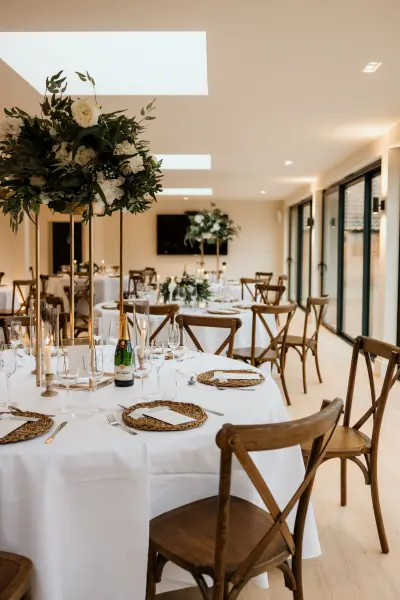 Elegant dining setup featuring white tablecloths, wooden chairs, and lush floral centerpieces, perfect for a sophisticated wedding reception.