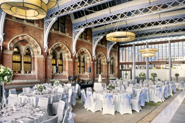 Expansive hall features stunning exposed brick walls, elegant round tables, and modern chandeliers, creating a sophisticated wedding atmosphere.