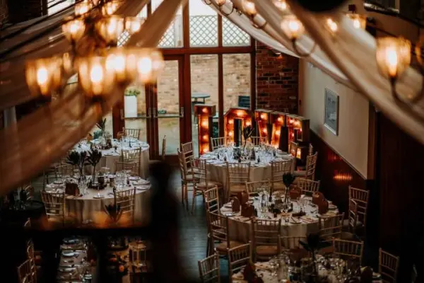 Charming indoor reception with elegant round tables, soft drapery, and warm lighting, creating a romantic atmosphere for celebrations.