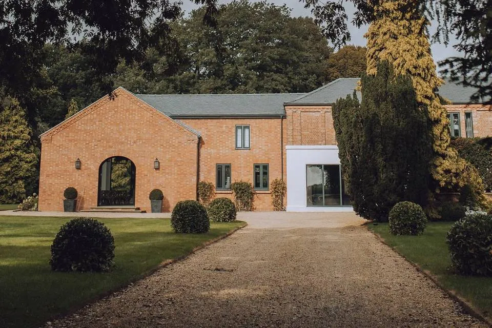 Charming brick venue with elegant arched entrance, lush gardens, and a winding gravel path, perfect for intimate wedding celebrations.