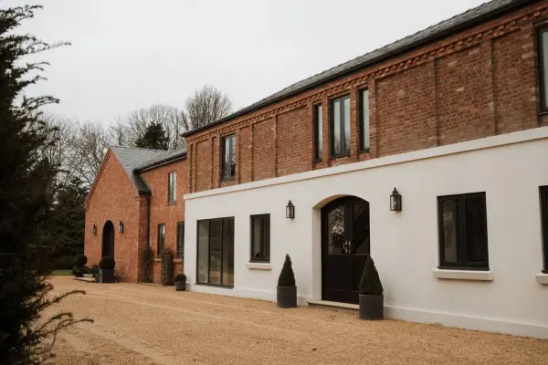 Charming rustic wedding venue featuring a brick exterior and modern white accents, surrounded by landscaped grounds and a gravel driveway.