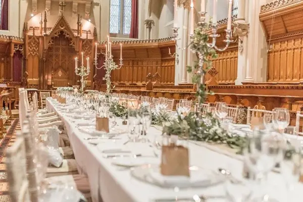Elegant reception setup with long tables adorned with greenery, candelabras, and fine dinnerware against a stunning wooden backdrop.