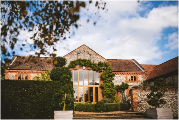 Charming stone barn with large windows, surrounded by manicured hedges and lush greenery, perfect for a romantic wedding setting.