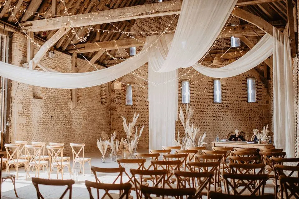 Rustic barn venue featuring elegant drapery, wooden chairs, and soft lighting, creating a warm, inviting atmosphere for ceremonies.