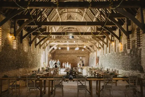 Rustic barn interior featuring exposed wooden beams, warm lighting, and elegantly set dining tables, perfect for a charming wedding celebration.