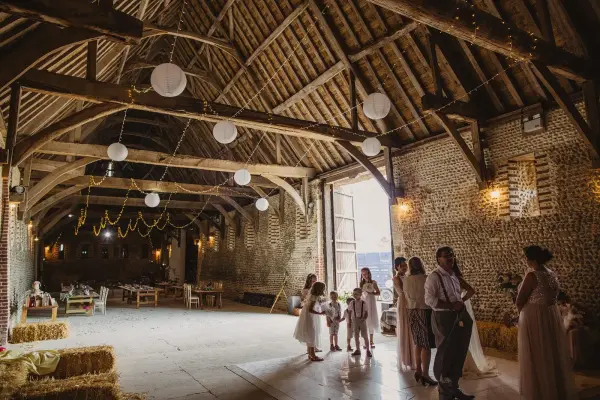 Rustic barn interior with exposed wooden beams, soft lighting, and straw bales, creating a warm and inviting space for a wedding celebration.