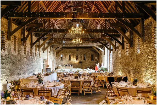 Elegant rustic barn featuring exposed beams, chandeliers, and beautifully arranged tables for a charming wedding reception.