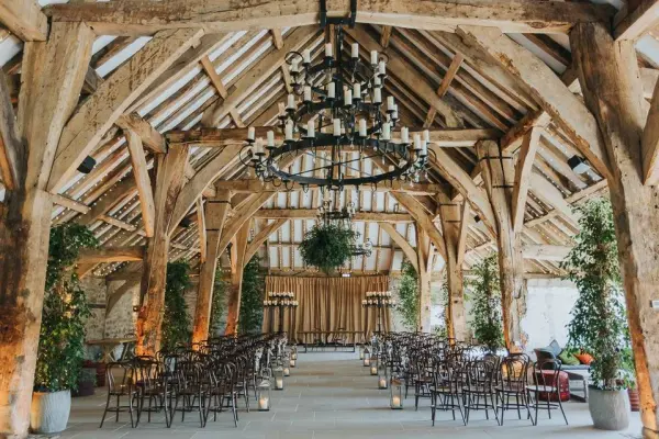 Rustic barn wedding venue featuring exposed wooden beams, elegant chandeliers, and lush greenery, creating a charming ceremony space.