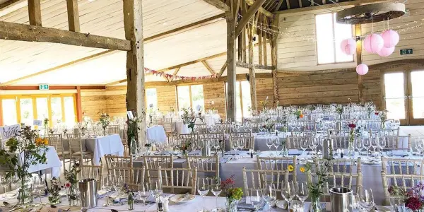 Bright and airy rustic barn venue featuring elegantly arranged tables with floral centerpieces, wooden beams, and soft pendant lighting.