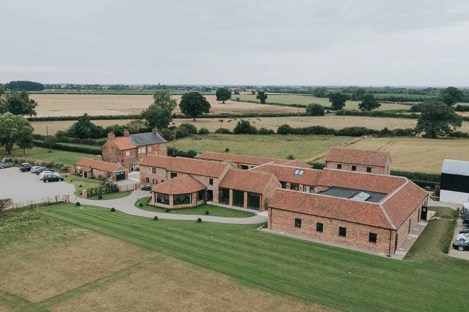 Aerial view of a rustic venue featuring charming brick buildings and lush green fields, perfect for outdoor wedding celebrations.