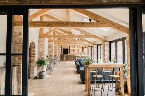 Spacious indoor venue featuring exposed wood beams, brick walls, and large windows, creating a warm and inviting atmosphere for gatherings.