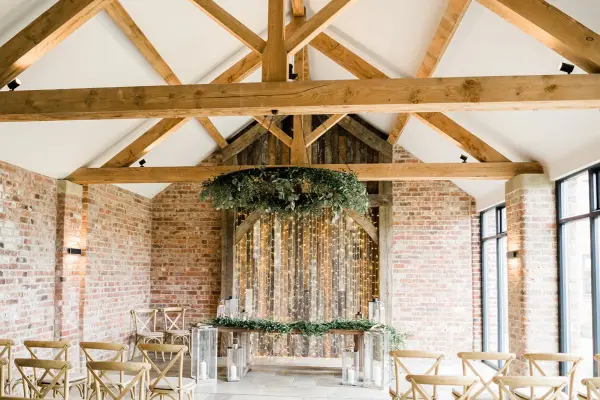 Charming indoor ceremony space featuring exposed wooden beams, rustic brick walls, and a charming greenery-adorned altar.