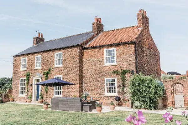 Charming rustic house with red brick exterior, green garden, and outdoor seating area, perfect for intimate weddings.