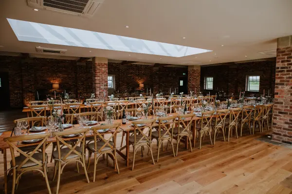 Rustic dining area featuring wooden crossback chairs, elegant tables, and warm brick walls with a skylight for natural light.