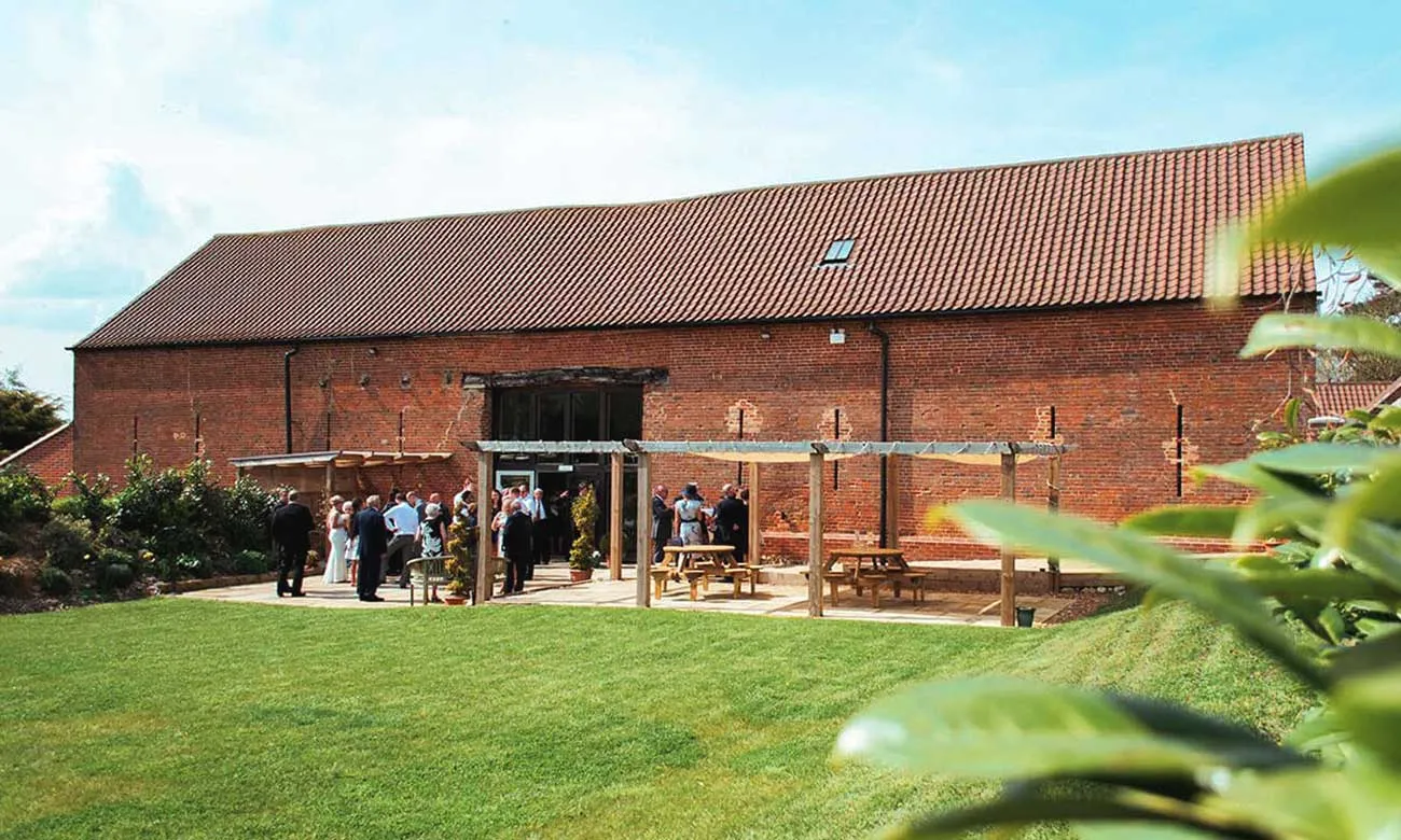 Rustic barn wedding venue with a spacious outdoor area, inviting guests to gather on manicured lawns under charming wooden Pergolas.
