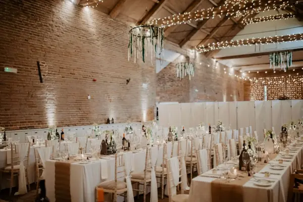 Rustic venue featuring elegant long tables adorned with soft linens, twinkling fairy lights, and warm brick walls for a charming atmosphere.