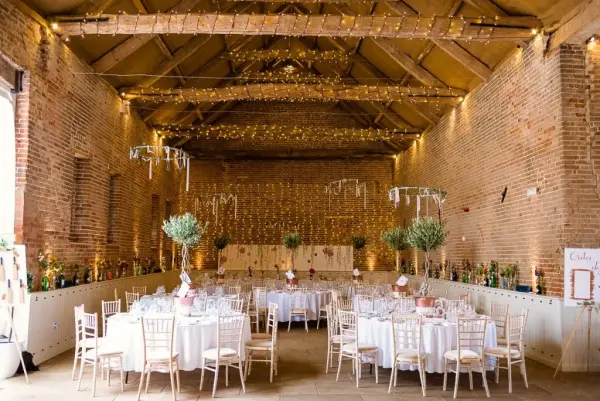Rustic barn venue featuring exposed brick walls, elegant round tables, lovely foliage accents, and warm string lights creating a cozy atmosphere.