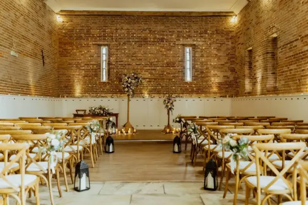 Intimate wedding ceremony space featuring warm brick walls, wooden chairs, and decorative lanterns lined along the aisle.