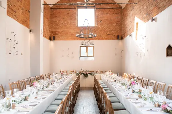 Charming reception hall with exposed brick walls, long banquet tables, and elegant chandeliers, perfect for intimate wedding celebrations.