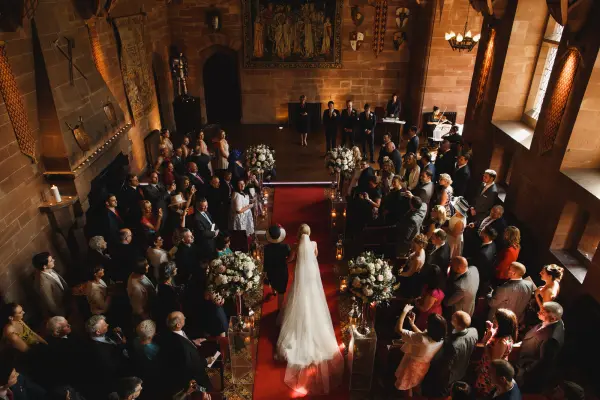 Elegant indoor ceremony with a red carpet aisle, surrounded by floral arrangements and stone walls, creating a romantic atmosphere.