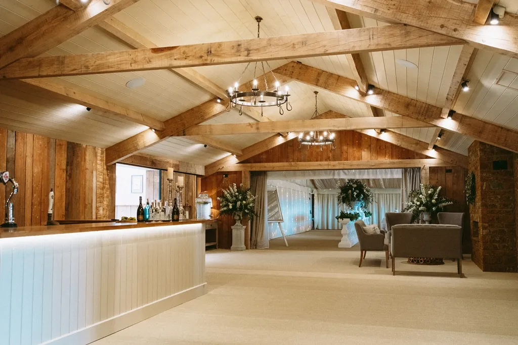 Rustic wedding venue featuring exposed wooden beams, elegant chandeliers, and a chic lounge area adorned with floral arrangements.