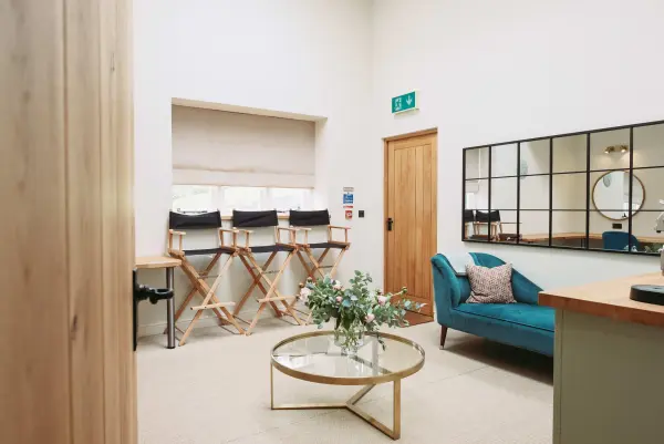 Bright, modern bridal suite featuring a cozy teal sofa, elegant mirror, and seating for wedding preparations, ideal for intimate gatherings.