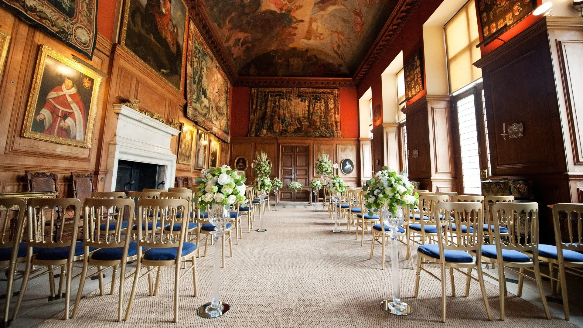 Opulent ceremony space featuring elegant wooden chairs, elaborate artwork, and floral arrangements, perfect for a romantic wedding setting.