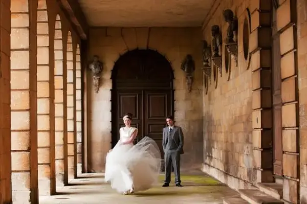 Couple stands elegantly in a grand stone corridor with archways, showcasing a historic backdrop for wedding photos.