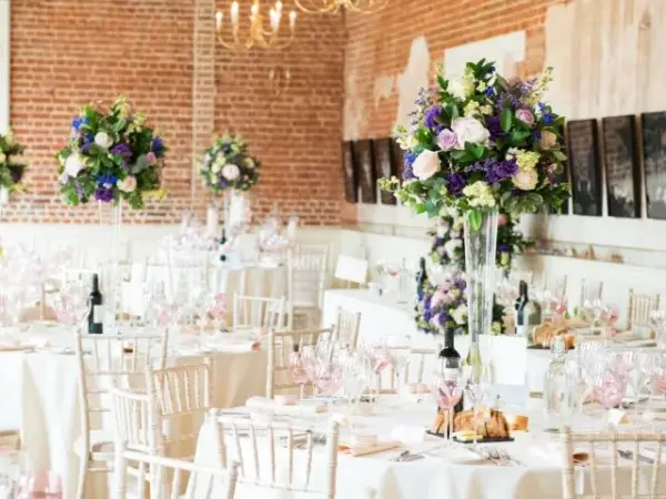 Rustic venue with exposed brick walls, elegant tables adorned with white linens, and towering floral centerpieces for a romantic ambiance.