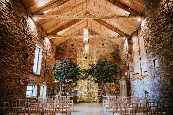 A charming rustic venue featuring exposed stone walls, wood beams, and elegant seating arranged for a romantic ceremony.