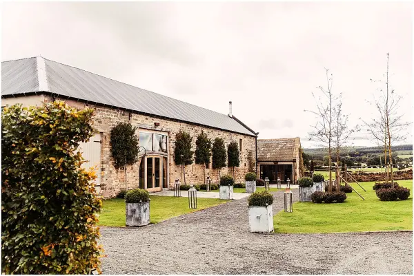 Charming rustic barn venue featuring manicured greenery, elegant planters, and scenic countryside views, ideal for intimate weddings.