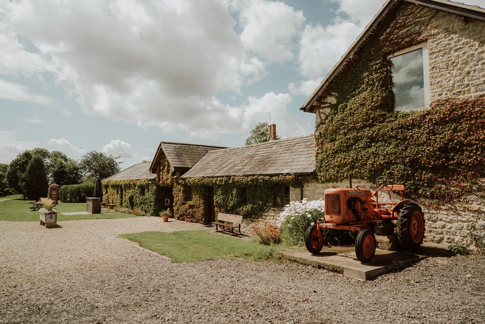 Charming rustic barn venue featuring ivy-covered stone walls, a vibrant red tractor, and a serene outdoor space ideal for weddings.