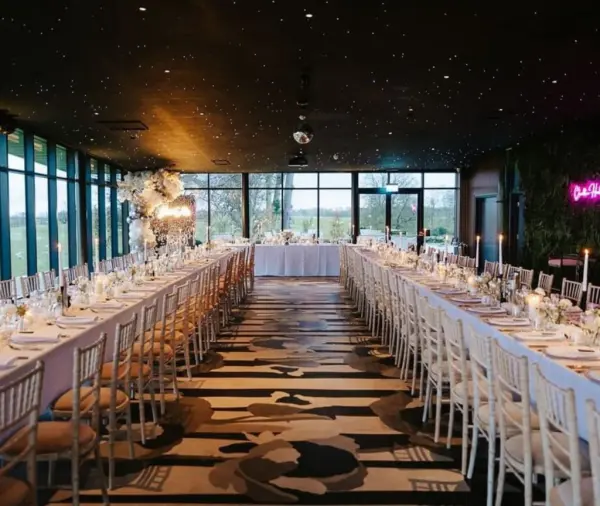 Elegant indoor reception space featuring long tables adorned with candles and floral arrangements, surrounded by panoramic windows.
