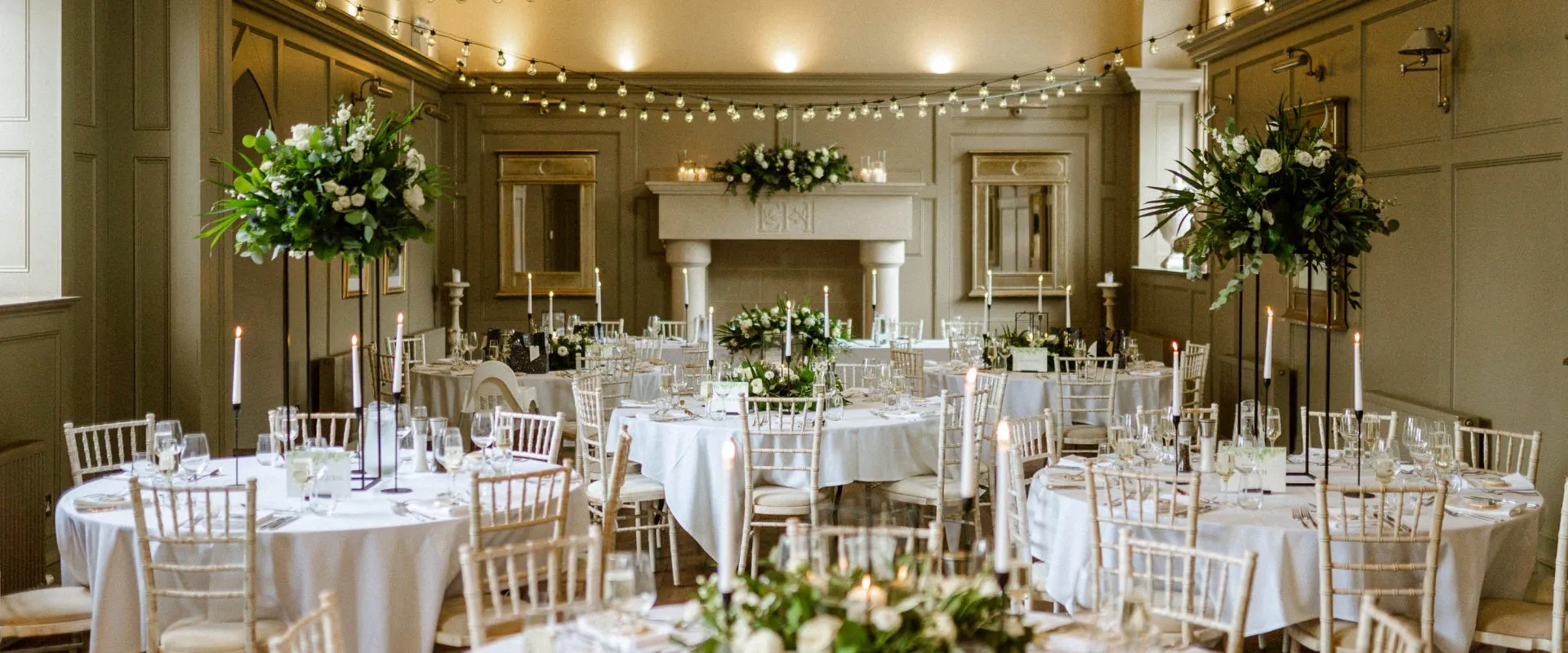 Elegant reception space featuring round tables adorned with floral centerpieces, candlelight, and softly lit walls for an intimate ambiance.