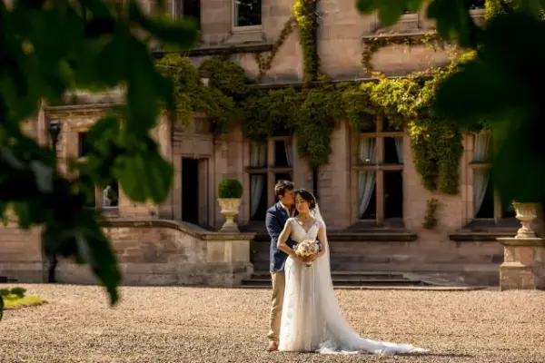A couple embraces in front of a charming stone manor adorned with ivy, highlighting romantic outdoor wedding charm.