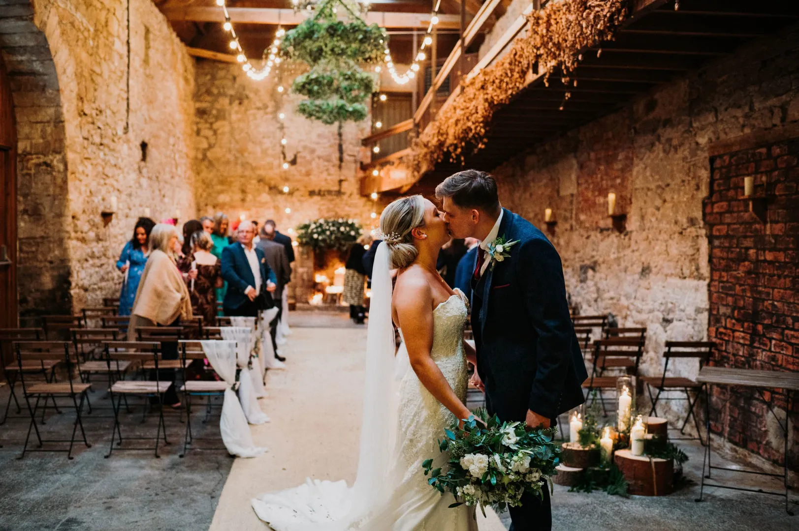 Charming rustic barn venue featuring exposed brick walls, hanging greenery, and candle-lit decor, ideal for intimate wedding ceremonies.